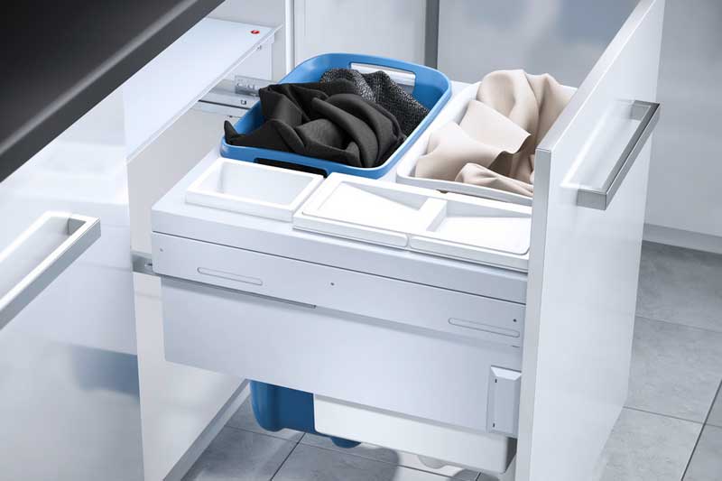 Ausziehbarer Schrank mit zwei Wäschesammlern in Blau, gefüllt mit dunkler und heller Wäsche, in modernem Hauswirtschaftsraum.